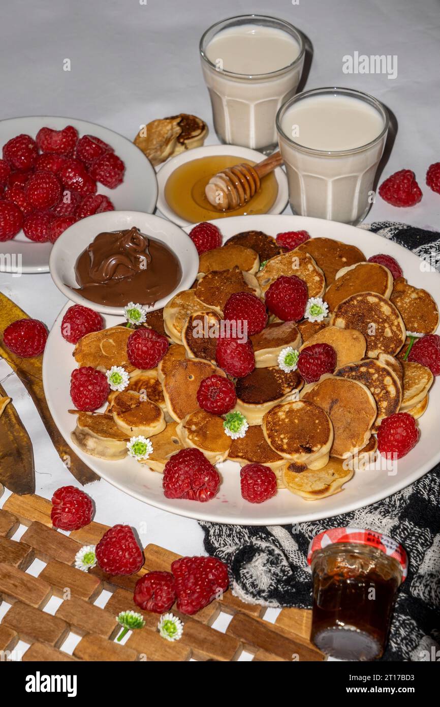Mini pancake serviti con miele, cioccolato, burro di arachidi e latte. Servizio fotografico con menu gastronomico. Scatto selettivo della messa a fuoco. Foto Stock