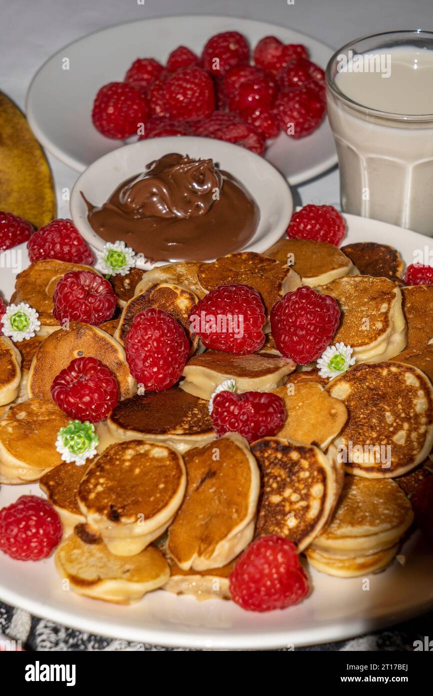 Mini pancake serviti con miele, cioccolato, burro di arachidi e latte. Servizio fotografico con menu gastronomico. Scatto selettivo della messa a fuoco. Foto Stock