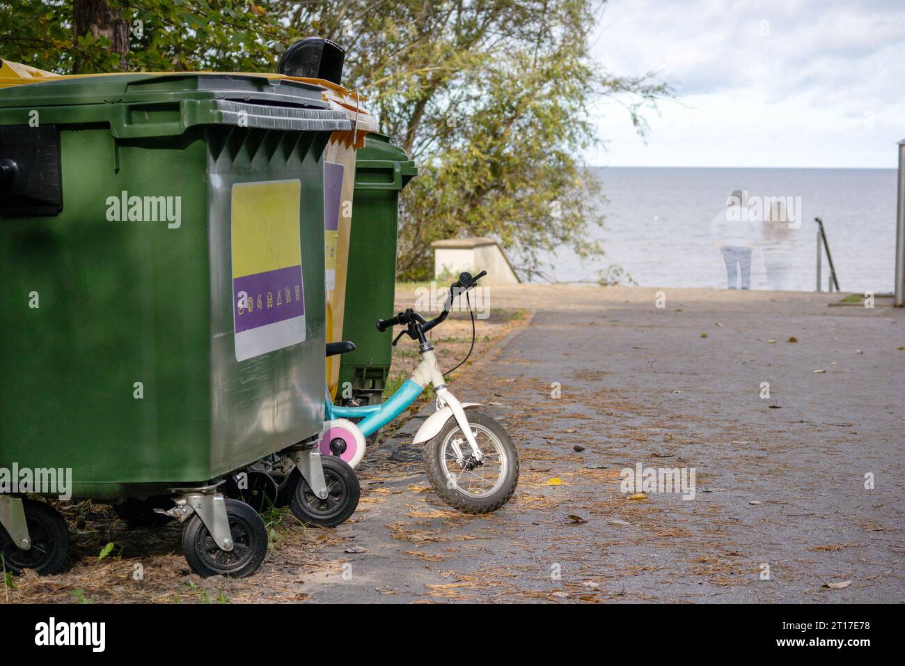 Contenitori per la spazzatura con una ruota per bambini collocata accanto a loro sullo sfondo del mare Foto Stock