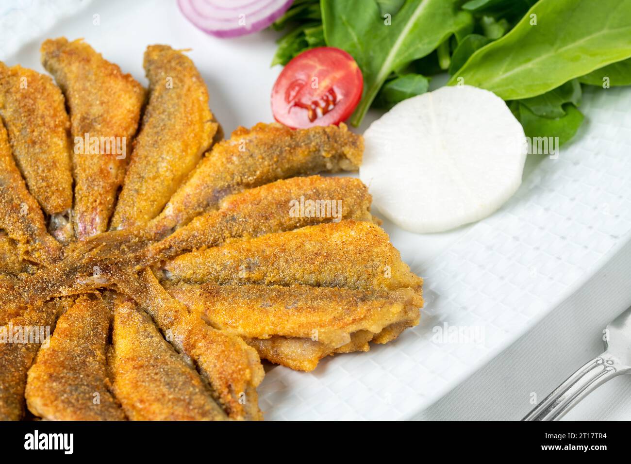 Mescolare le acciughe fritte con verdure fresche, pomodori e cipolle su un piatto di porcellana bianca Foto Stock