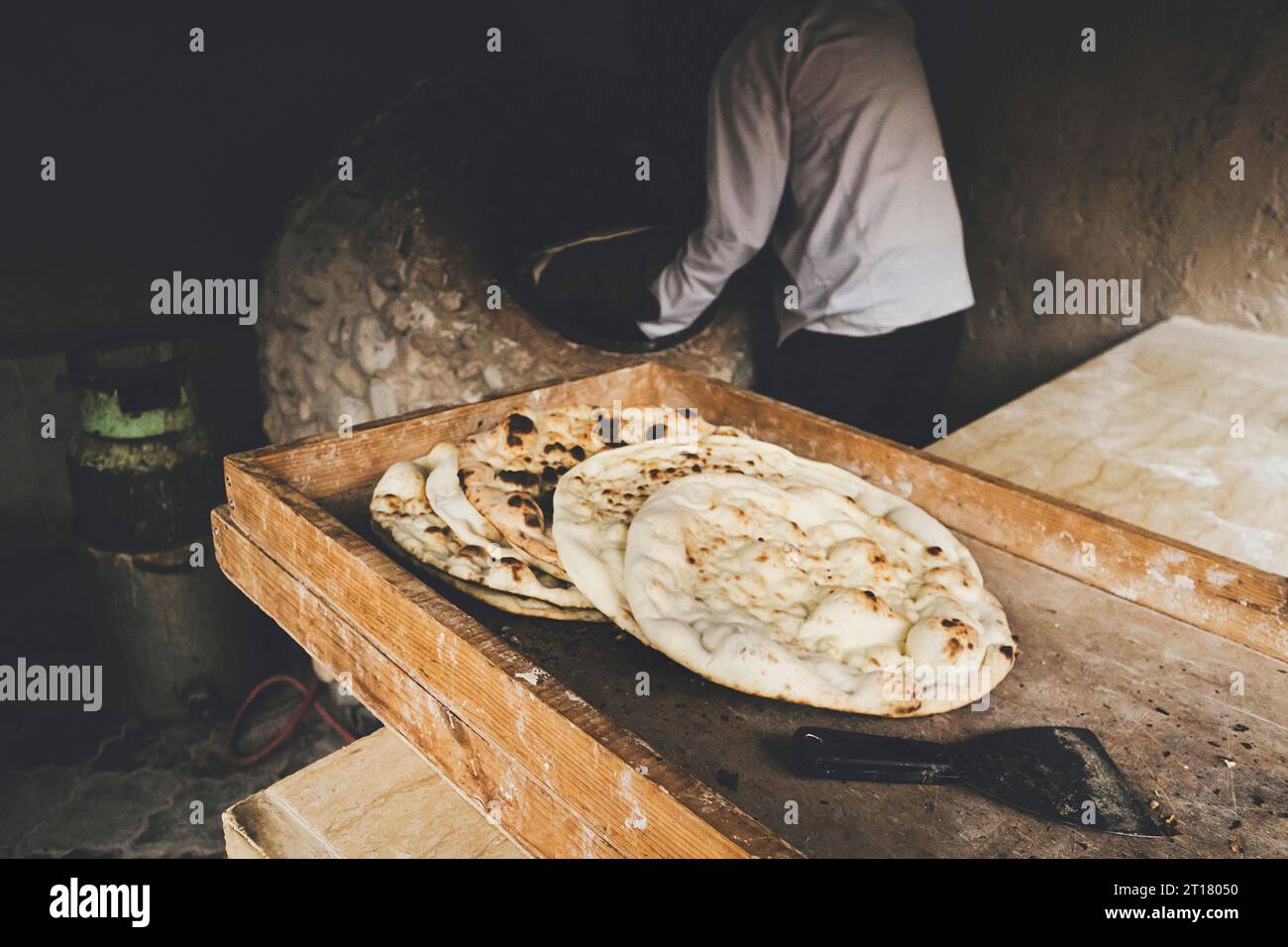 l'uomo invecchiato fa il pane tradizionale nel vecchio forno rotondo della pietra nel villaggio rurale. Cucina dell'Asia centrale. Pane caldo. Foto Stock