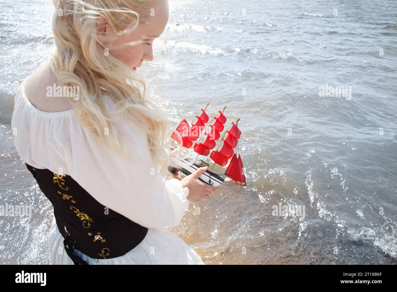 Bella giovane donna che regge yacht con vele rosse e si trova sulla spiaggia di mare all'aperto, romantico concetto di viaggio Foto Stock