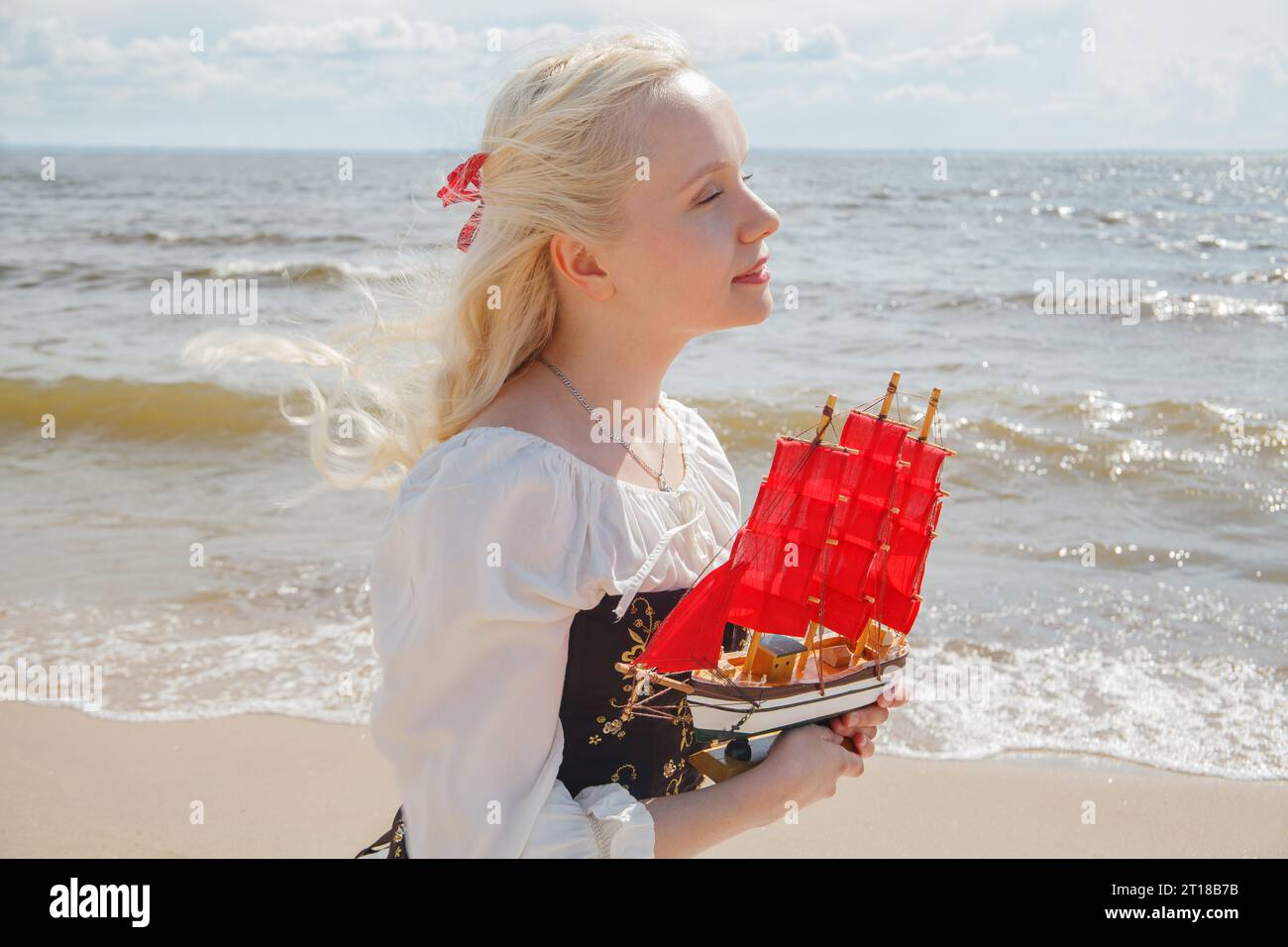 Giovane donna con i capelli biondi che indossa un abito retrò che sogna sulla spiaggia di mare, ritratto all'aperto Foto Stock