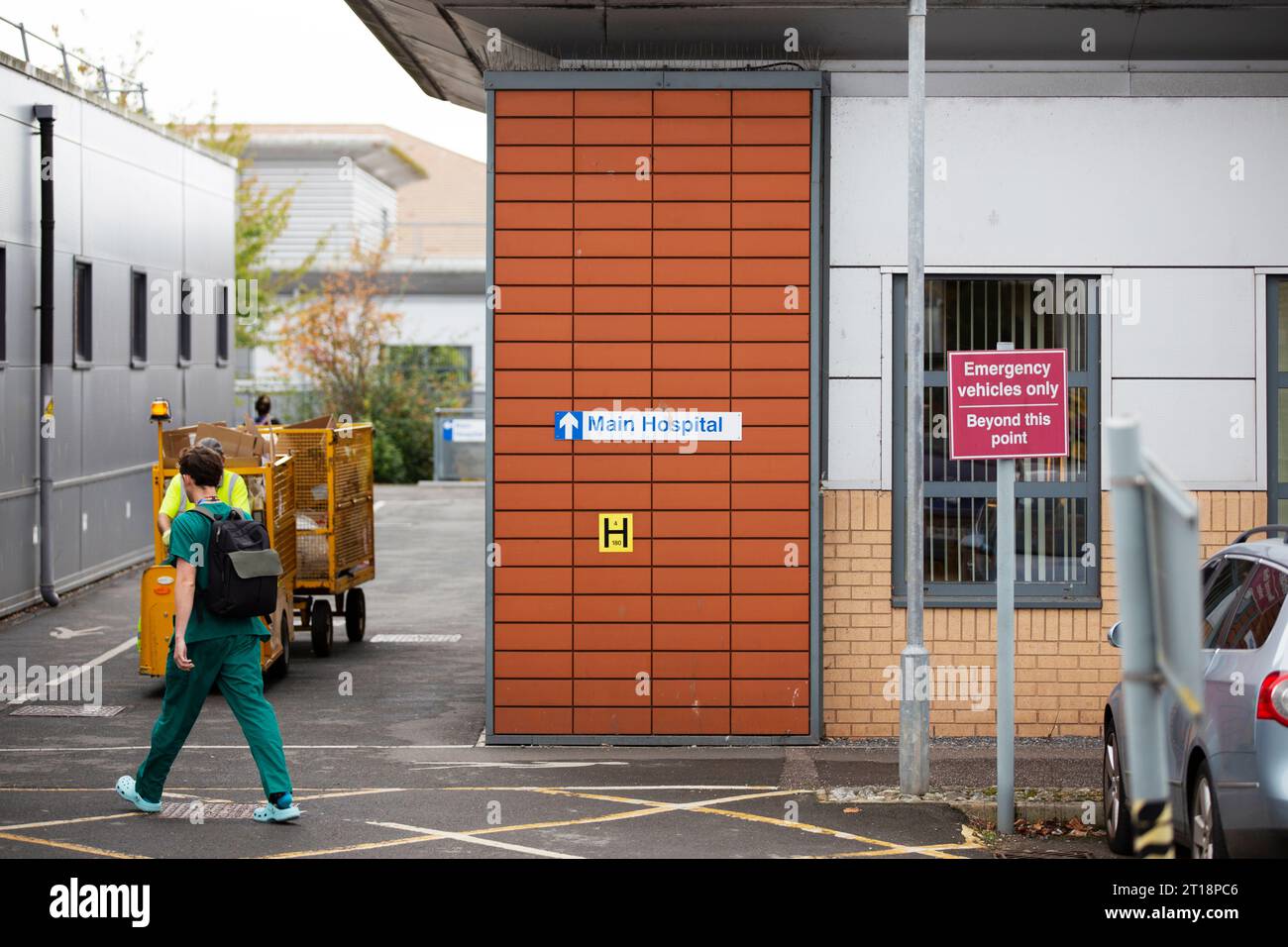 Verde uniforme uomo / medico / medico professionista o consulente andare in ospedale principale e camminare oltre segno a Exeter ospedale R S & E. Foto Stock