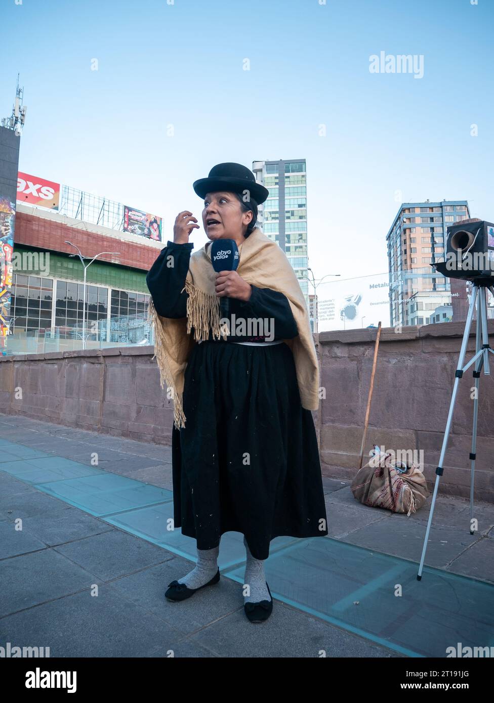 La Paz, Bolivia - 8 agosto 2022: Donna indigena boliviana vestita con costumi tradizionali accanto a una macchina fotografica in cartone e a un treppiede Foto Stock