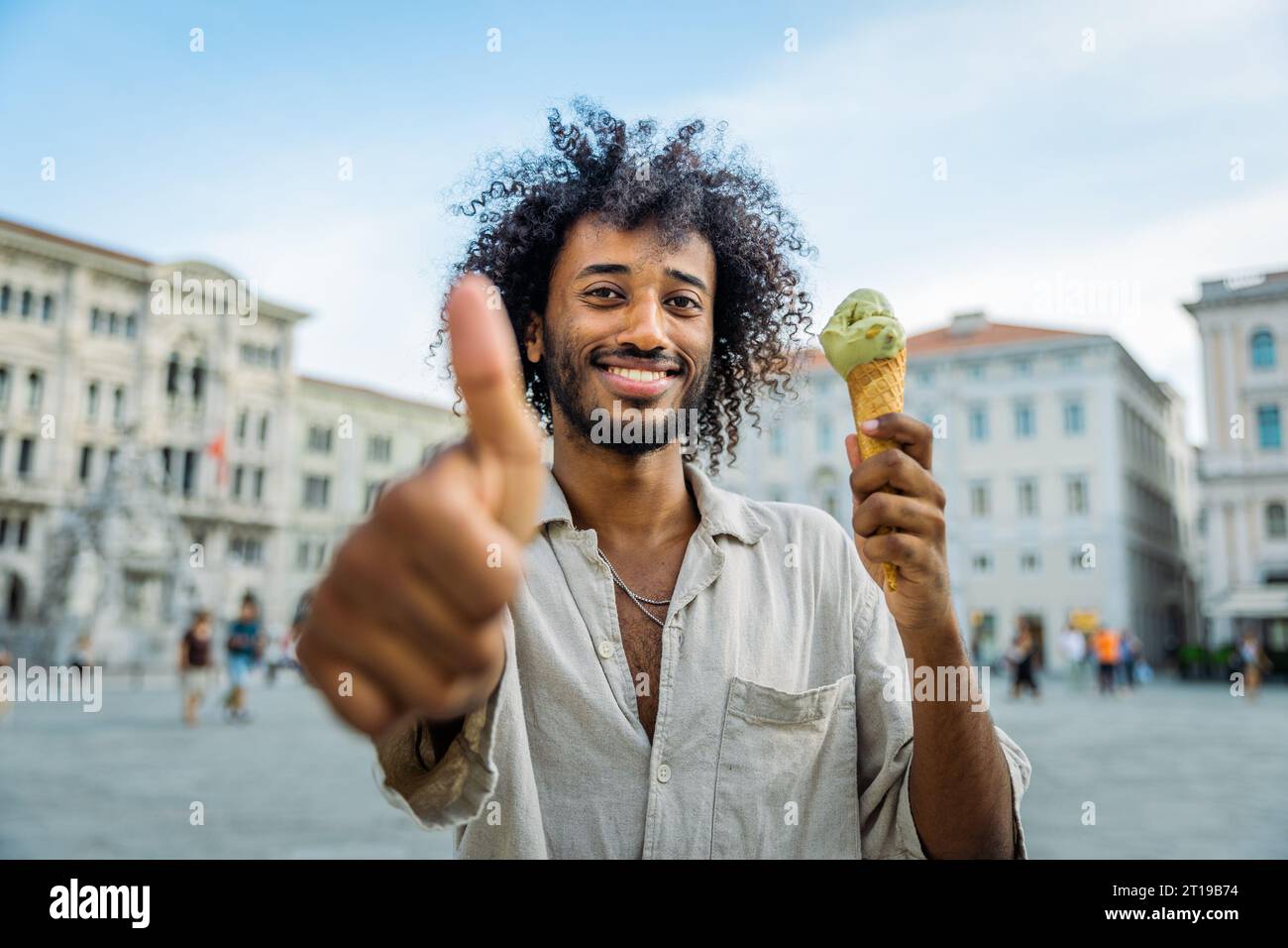 Un uomo è felice e mostra un pollice in alto mentre mangia un gelato Foto Stock