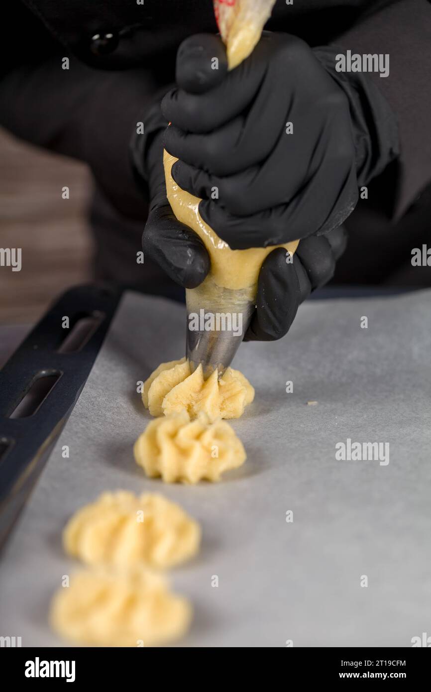 Un individuo con guanti neri spreme l'impasto da un sacchetto di pasticceria per preparare i biscotti utilizzando un sacchetto di pasticceria Foto Stock