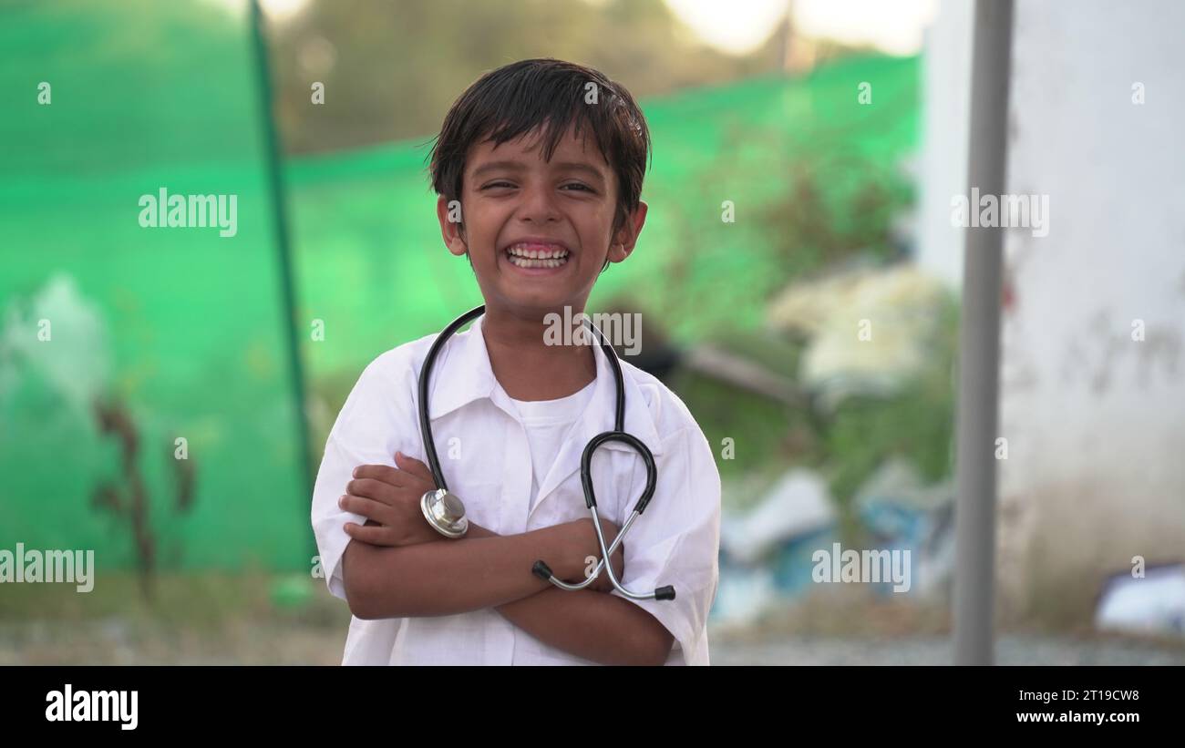 Carino bambino indiano piccolo indossa uniforme medica tenendo stetoscopio che gioca medico, felice divertente piccolo misto razza bambino prescolare fingendo pediatrici Foto Stock