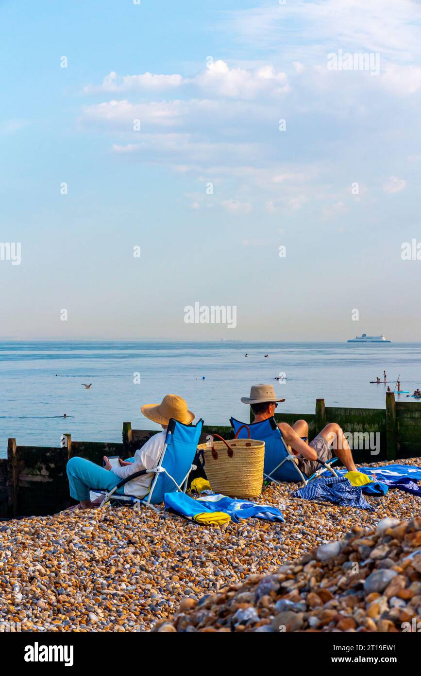 Coppia su sdraio leggendo e prendendo il sole a Kingsdown Beach nel Kent Inghilterra Regno Unito con l'herpes zoster in primo piano e una grande nave all'orizzonte. Foto Stock