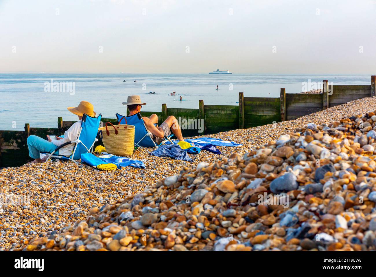 Coppia su sdraio leggendo e prendendo il sole a Kingsdown Beach nel Kent Inghilterra Regno Unito con l'herpes zoster in primo piano e una grande nave all'orizzonte. Foto Stock