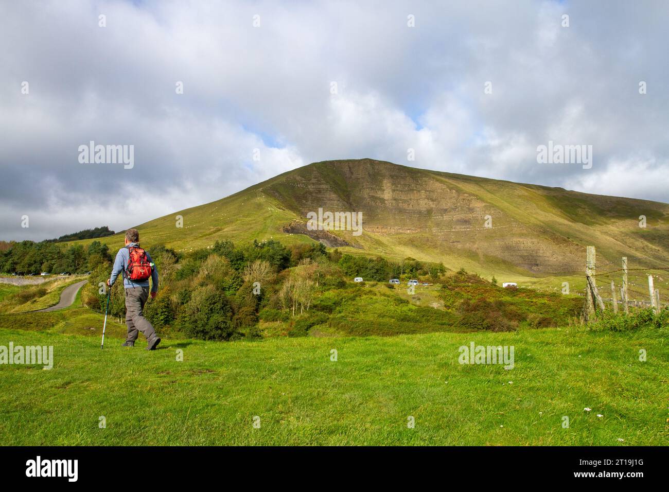 Un uomo che si trova in una collina da zaino in spalla e che cammina nel Peak District, sopra il villaggio del Derbyshire di Castleton, con la Great Ridge e la MAM Tor in lontananza Foto Stock