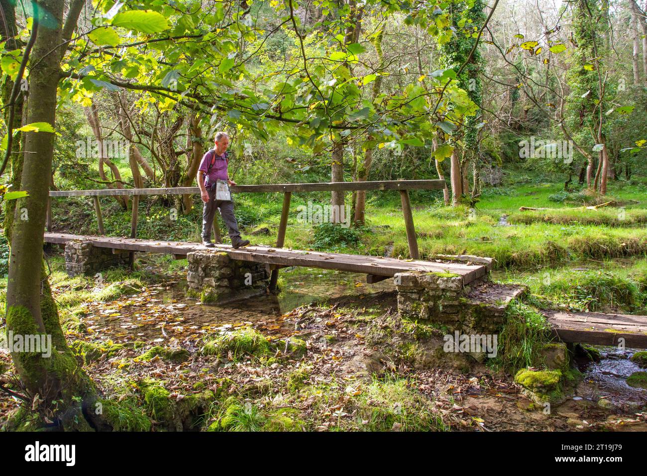 Uomo che cammina con zaino in spalla sul ponte pedonale all'estremità Miller's Dale di Monk's Dale, nel Peak District National Park Foto Stock