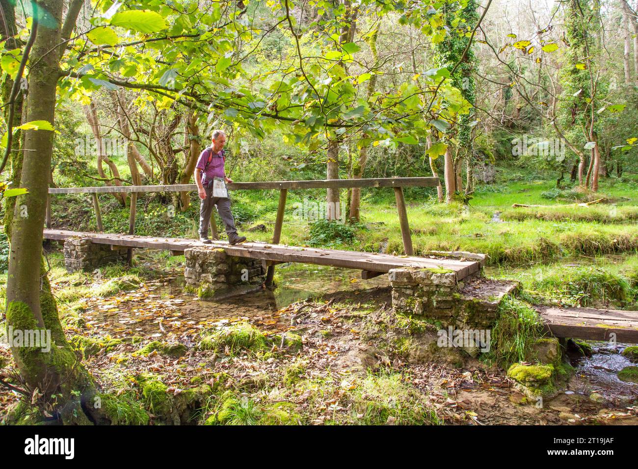 Uomo che cammina con zaino in spalla sul ponte pedonale all'estremità Miller's Dale di Monk's Dale, nel Peak District National Park Foto Stock