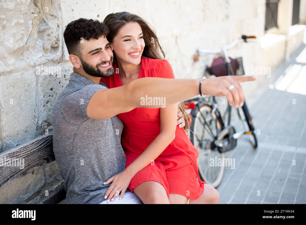 Giovane coppia sorridente e felice. Seduto su una panchina accanto a una bicicletta. Foto Stock