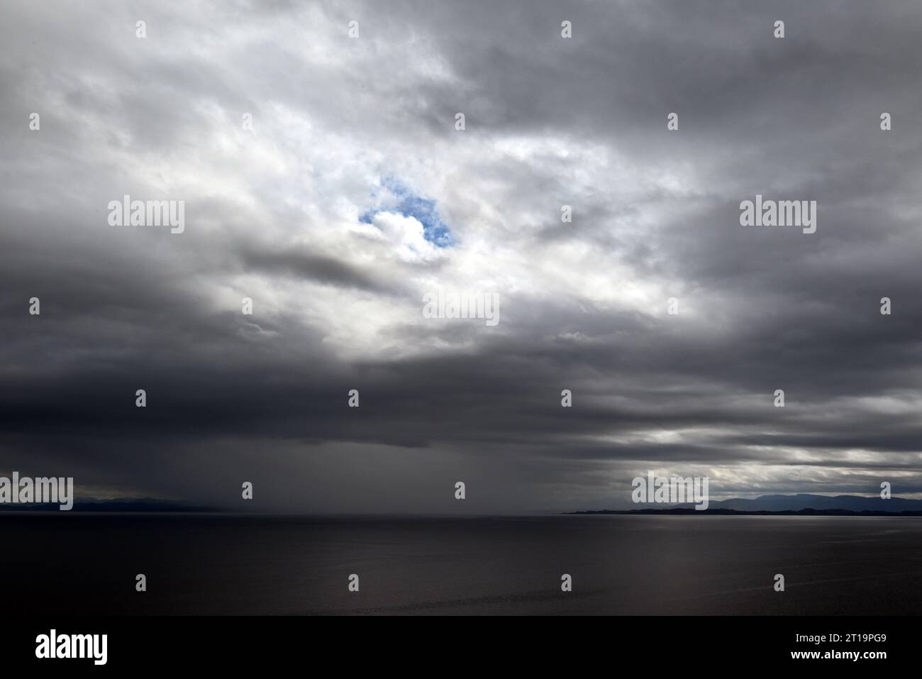 Una tempesta che si avvicina con nuvole nere sulla costa delle isole di Skye, in Scozia. Un foro blu attraverso le nuvole è ancora visibile. Foto Stock