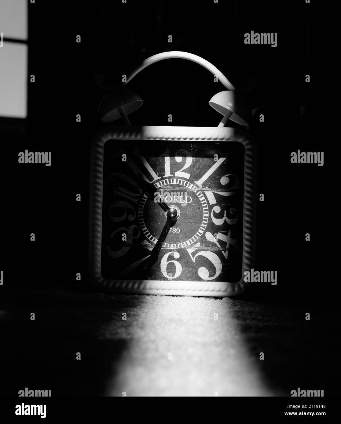 Fotografia in bianco e nero di un orologio analogico in una stanza buia con luce solare che illumina metà del suo volto. Foto Stock