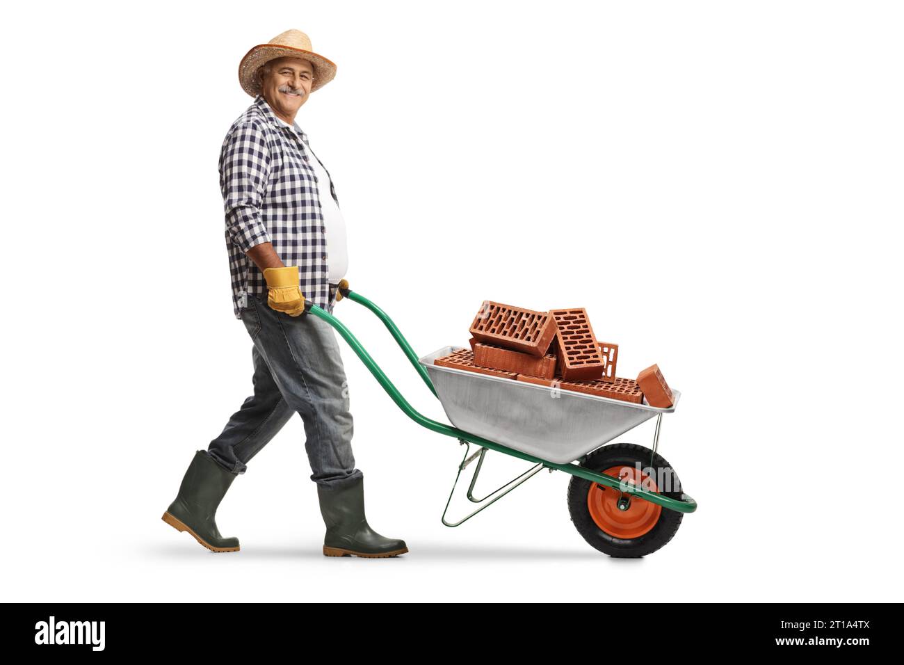Foto a profilo completo di un giardiniere maturo che spinge una carriola con mattoni isolati su sfondo bianco Foto Stock