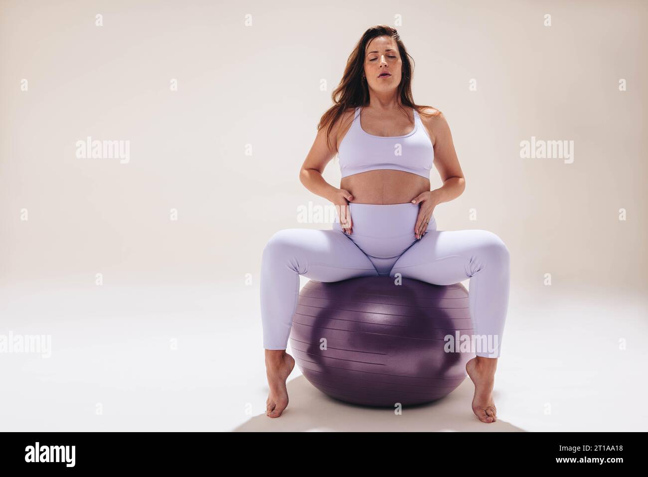 La mamma pratica yoga prenatale, utilizzando una palla di stabilità per l'esercizio fisico e la flessibilità. Con un'attenta respirazione e un abbigliamento fitness, dà la priorità Foto Stock