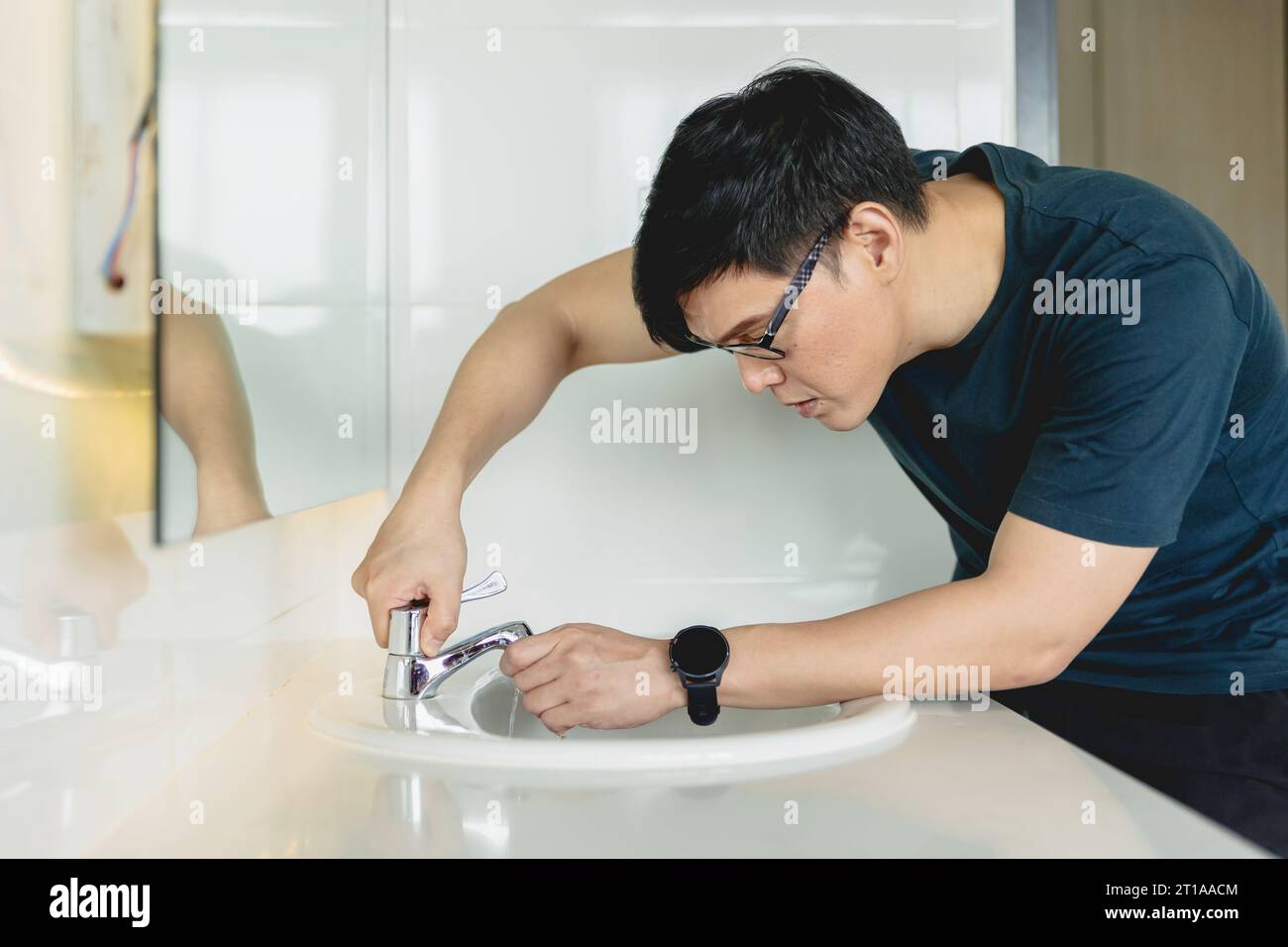 l'uomo ripara il lavandino del bagno, il rubinetto del rubinetto del tubo del rubinetto perde il marito che lavora come tuttofare a casa. Foto Stock