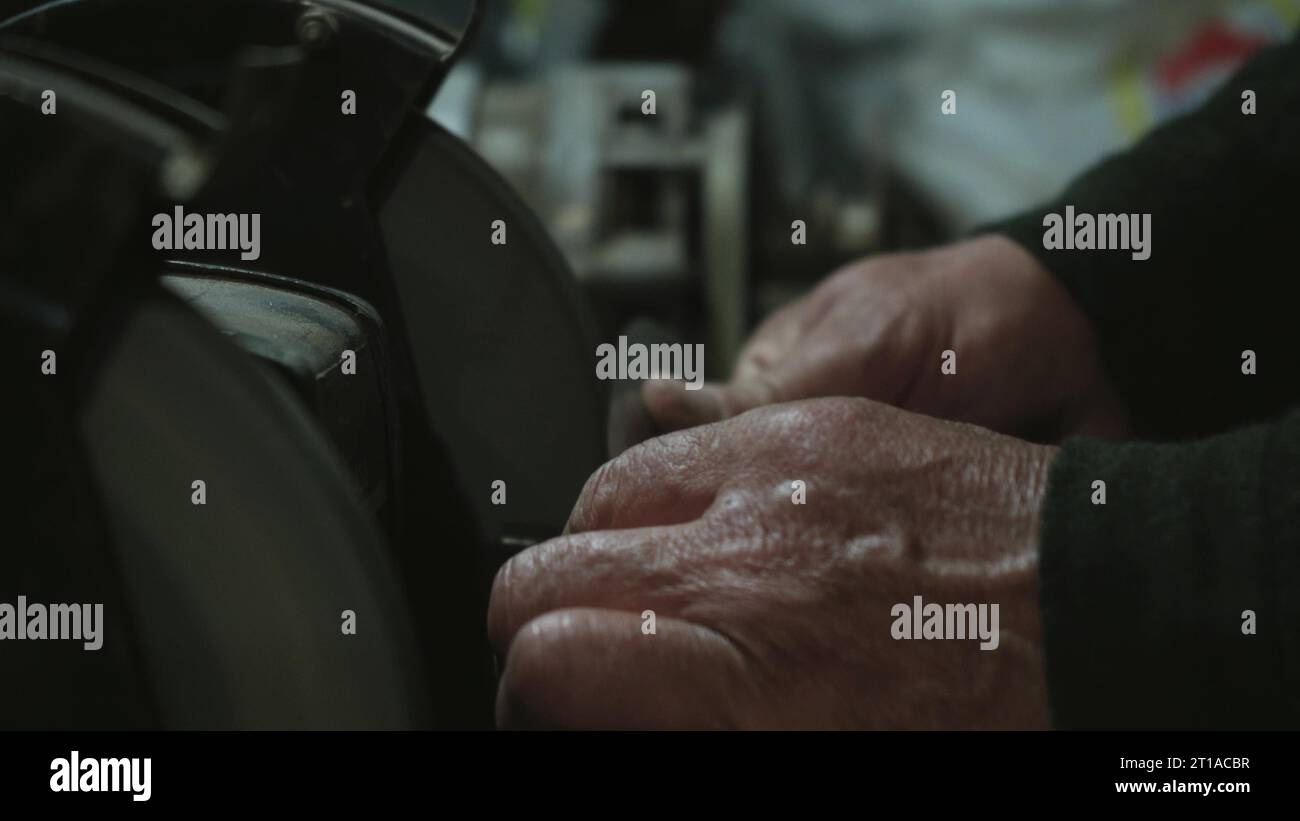 Le mani degli uomini lavorano a una macchina. Le scintille volano dal metallo caldo. L'uomo ha lavorato duramente sull'acciaio. Affilatura a macchina su una smerigliatrice elettrica, affilatura manuale o Foto Stock