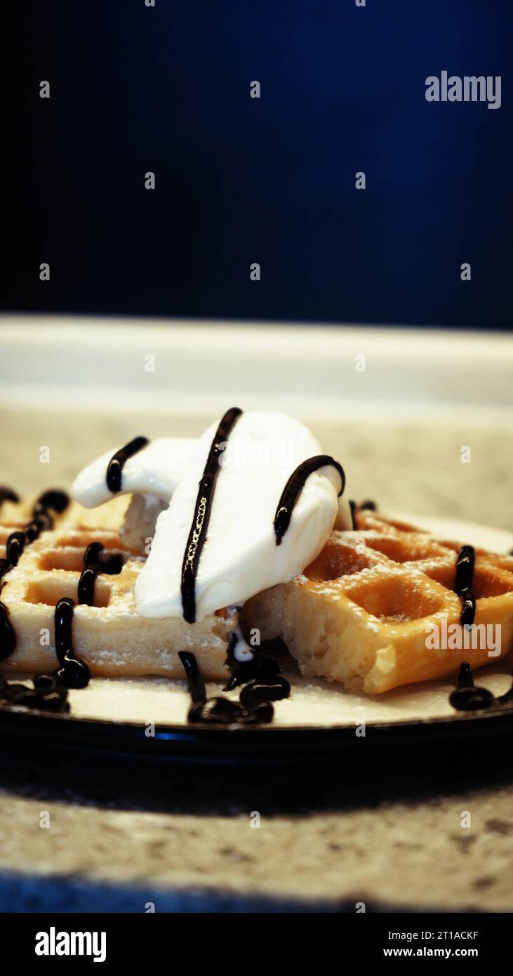 Condire i soffici waffle belgi con un condimento di cioccolato mentre prepari il dessert. Preparazione di dolci da waffle morbidi e gelati dolci Foto Stock