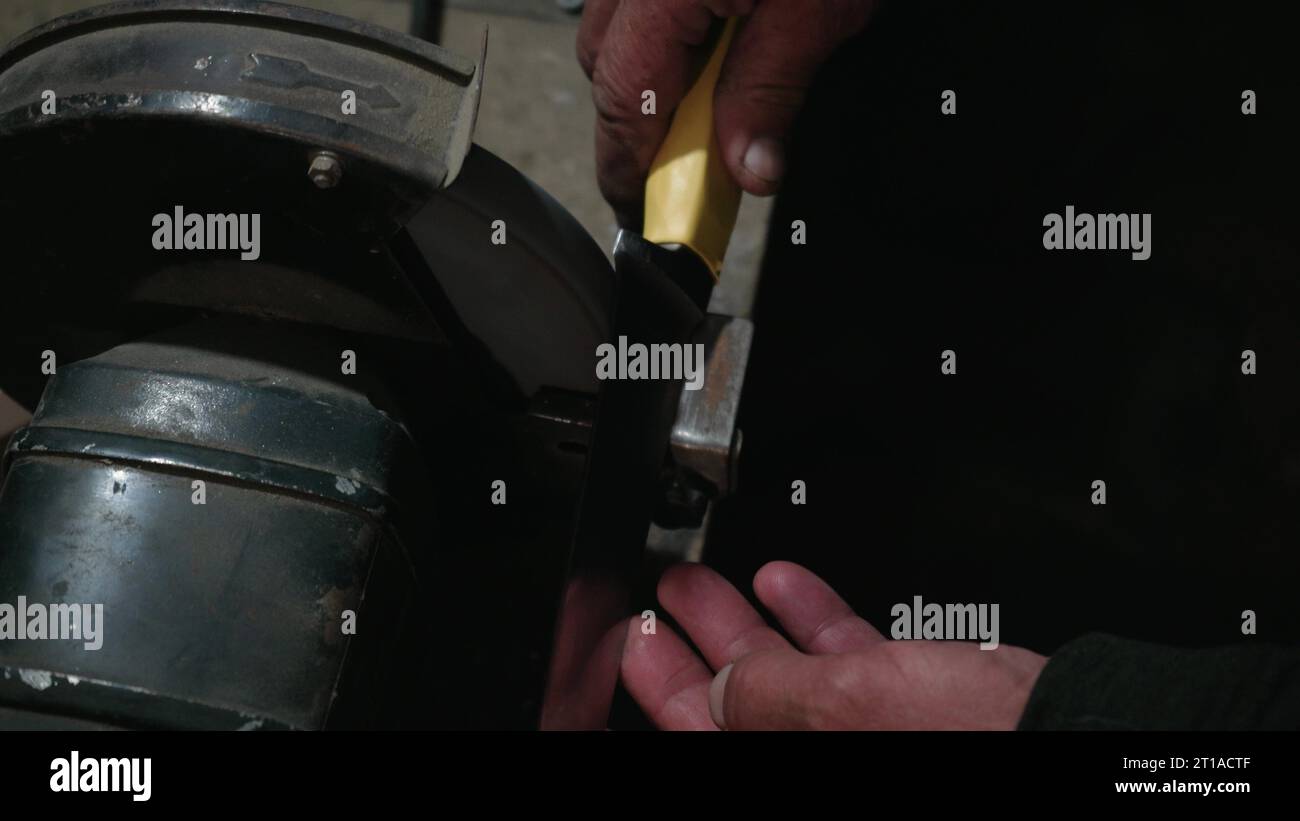 Le mani degli uomini lavorano a una macchina. Le scintille volano dal metallo caldo. L'uomo ha lavorato duramente sull'acciaio. Affilatura a macchina su una smerigliatrice elettrica, affilatura manuale o Foto Stock
