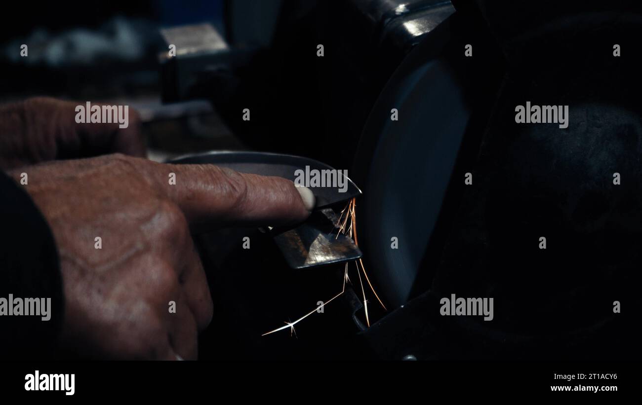 Le mani degli uomini lavorano a una macchina. Le scintille volano dal metallo caldo. L'uomo ha lavorato duramente sull'acciaio. Affilatura a macchina su una smerigliatrice elettrica, affilatura manuale o Foto Stock