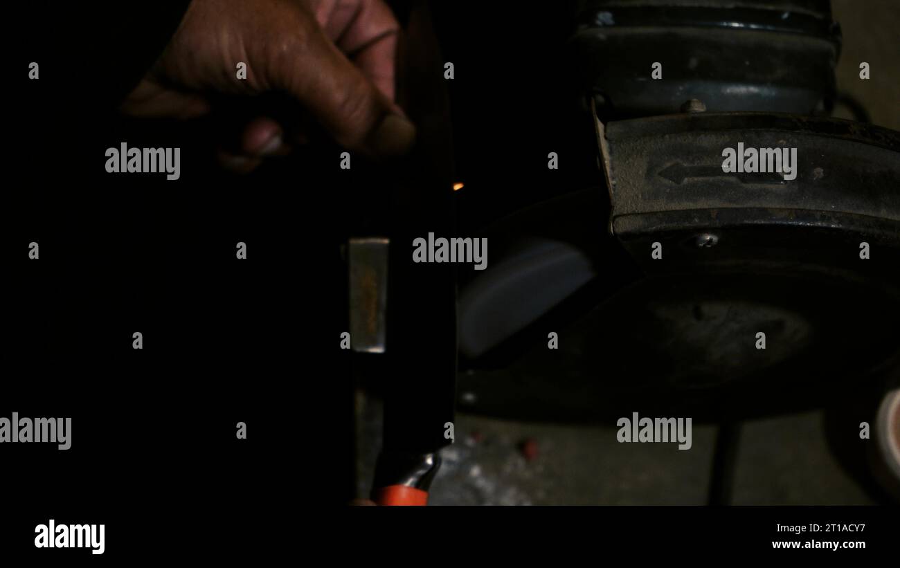 Le mani degli uomini lavorano a una macchina. Le scintille volano dal metallo caldo. L'uomo ha lavorato duramente sull'acciaio. Affilatura a macchina su una smerigliatrice elettrica, affilatura manuale o Foto Stock