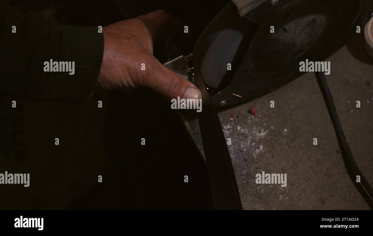 Le mani degli uomini lavorano a una macchina. Le scintille volano dal metallo caldo. L'uomo ha lavorato duramente sull'acciaio. Affilatura a macchina su una smerigliatrice elettrica, affilatura manuale o Foto Stock