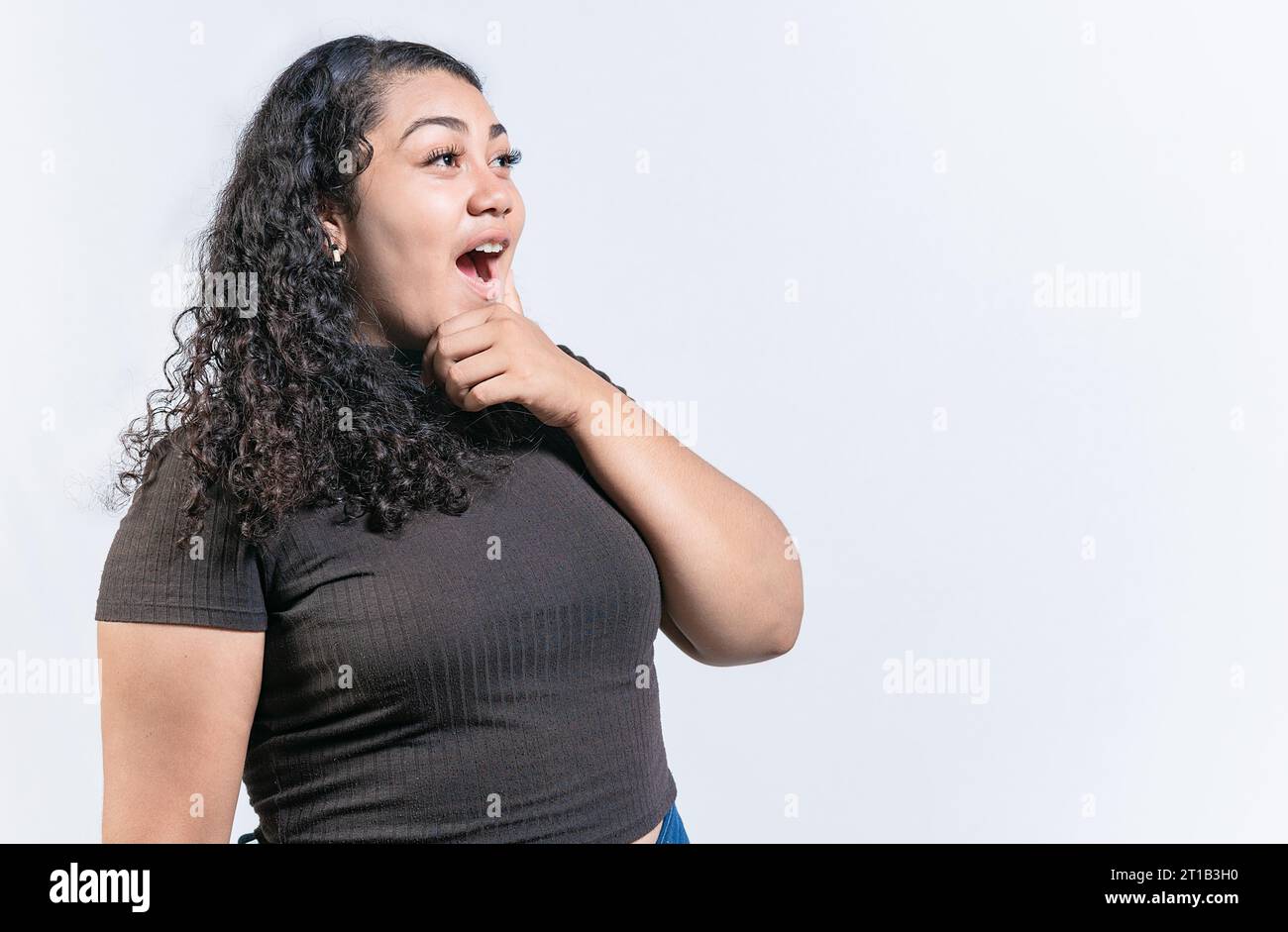 Una donna sorpresa che tiene il mento guardando una pubblicità a Side. Stupita donna latina con la mano sul mento che guarda il lato isolato Foto Stock