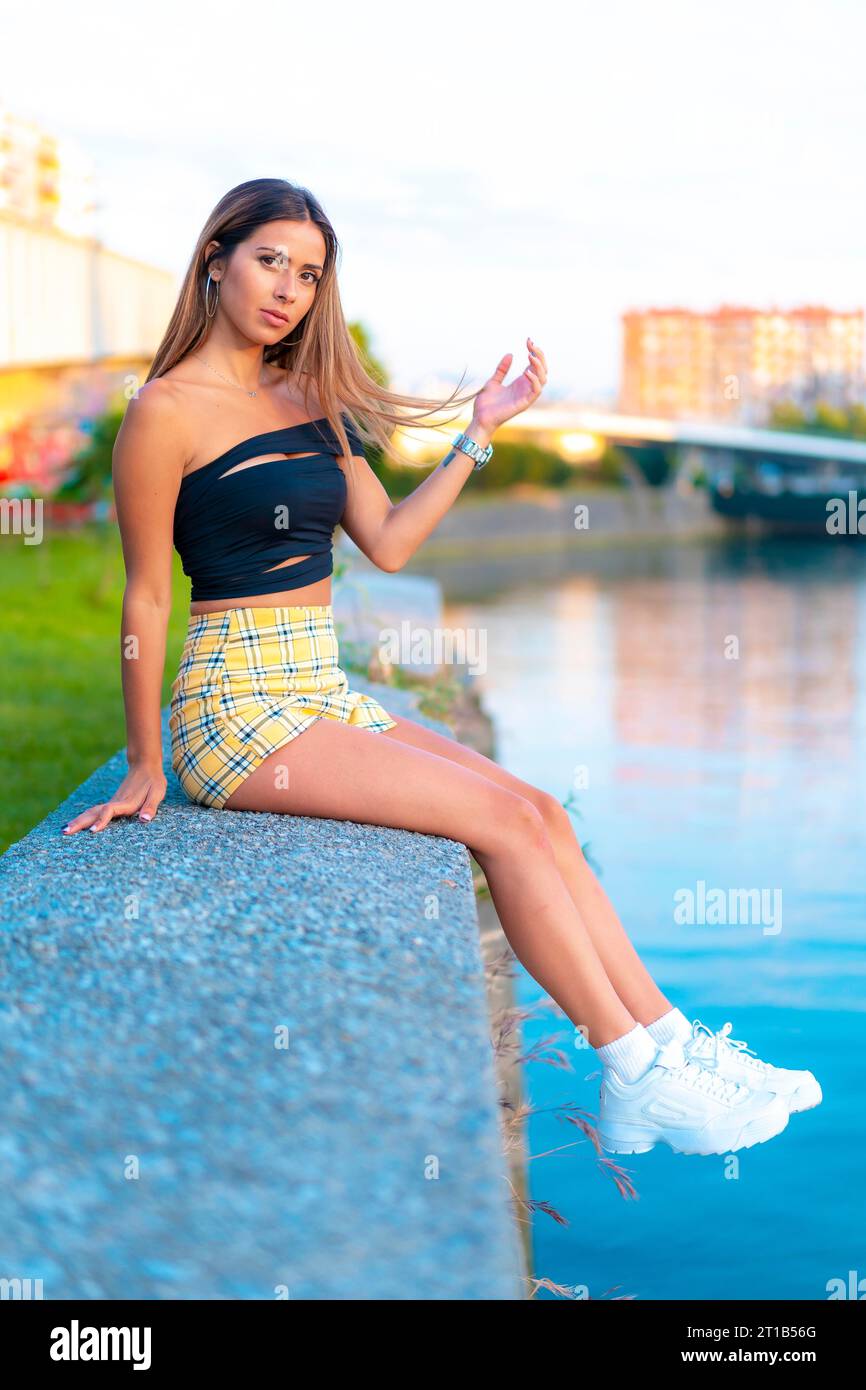 Lifestyle, una giovane donna caucasica dai capelli scuri seduta sul fiume della città Foto Stock