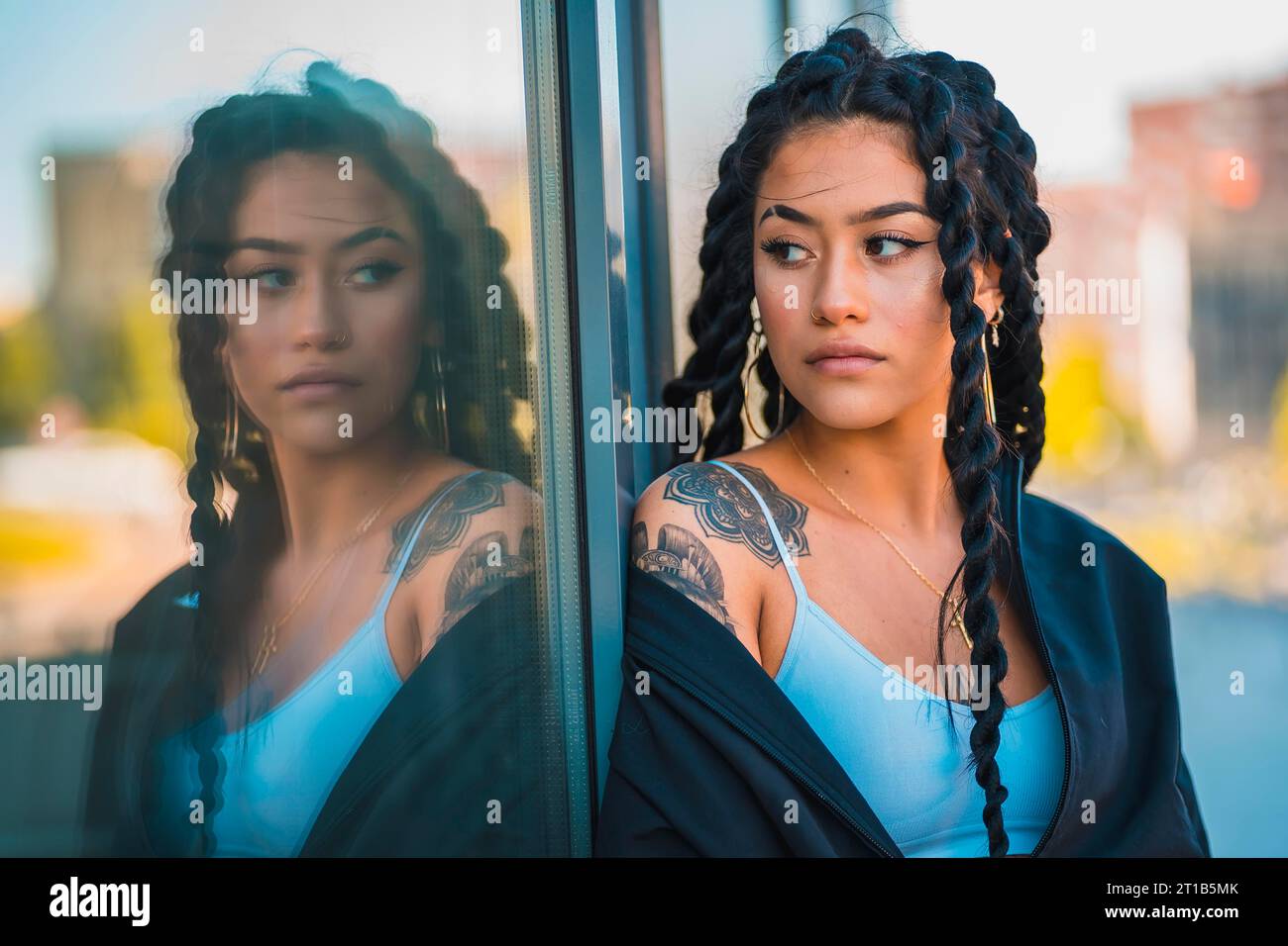 Sessione urbana. Giovane donna di etnia nera con lunghe trecce e tatuaggi, vetro, aspetto Foto Stock