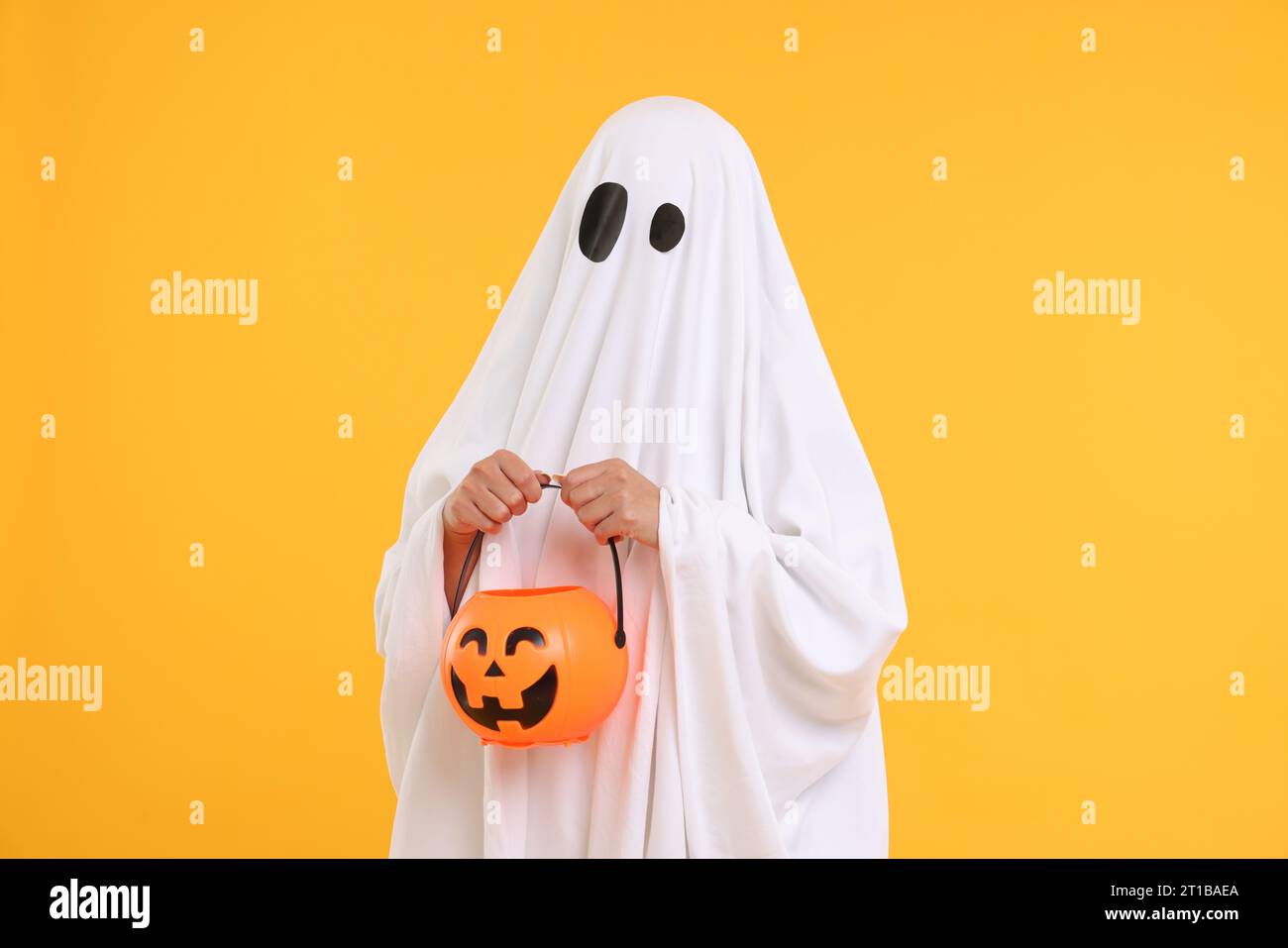 Donna in costume fantasma bianco con secchio di zucca su sfondo giallo. Festa di Halloween Foto Stock
