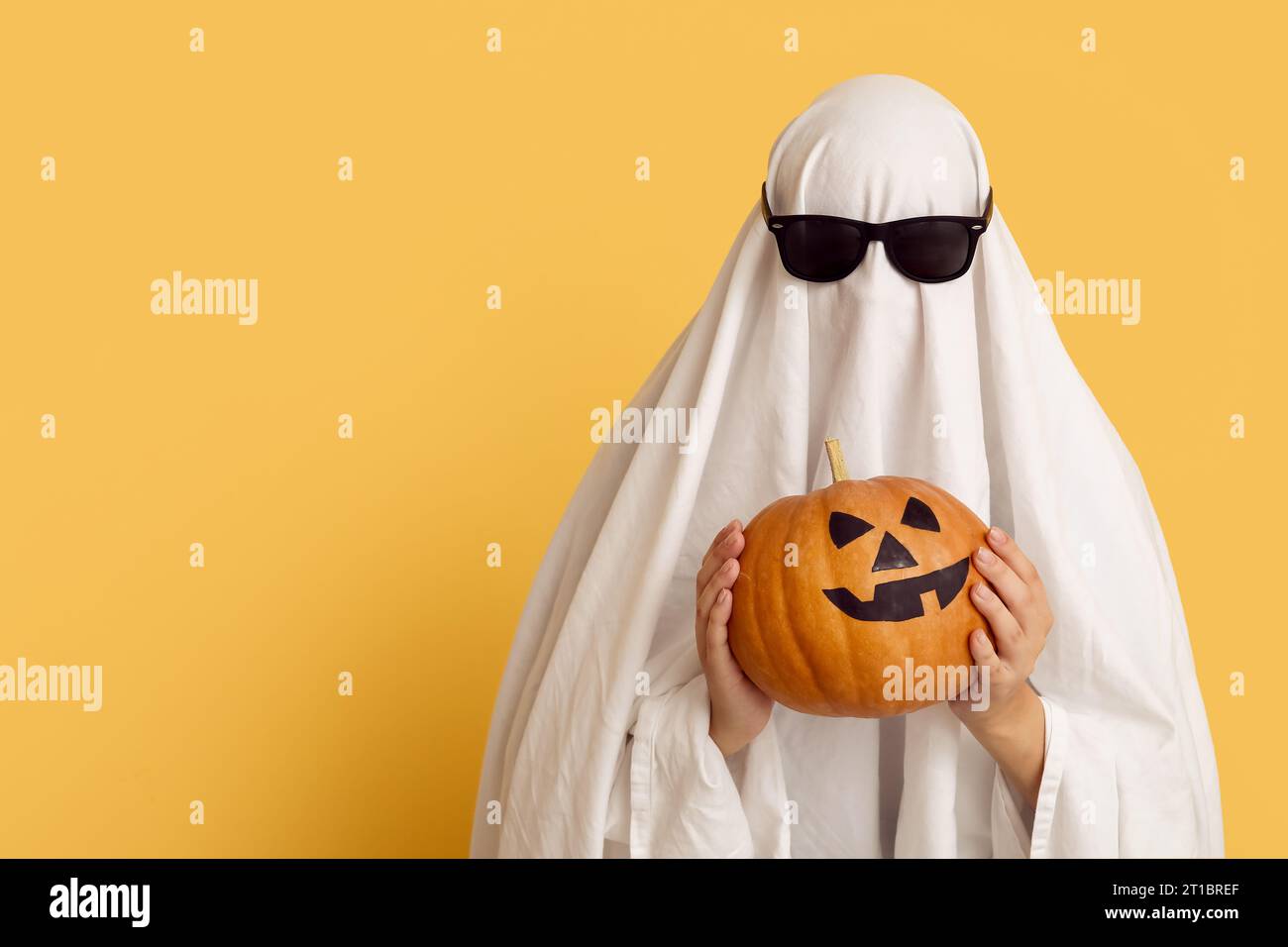 Donna in costume di Halloween con fantasma e occhiali da sole con zucca su sfondo colorato Foto Stock