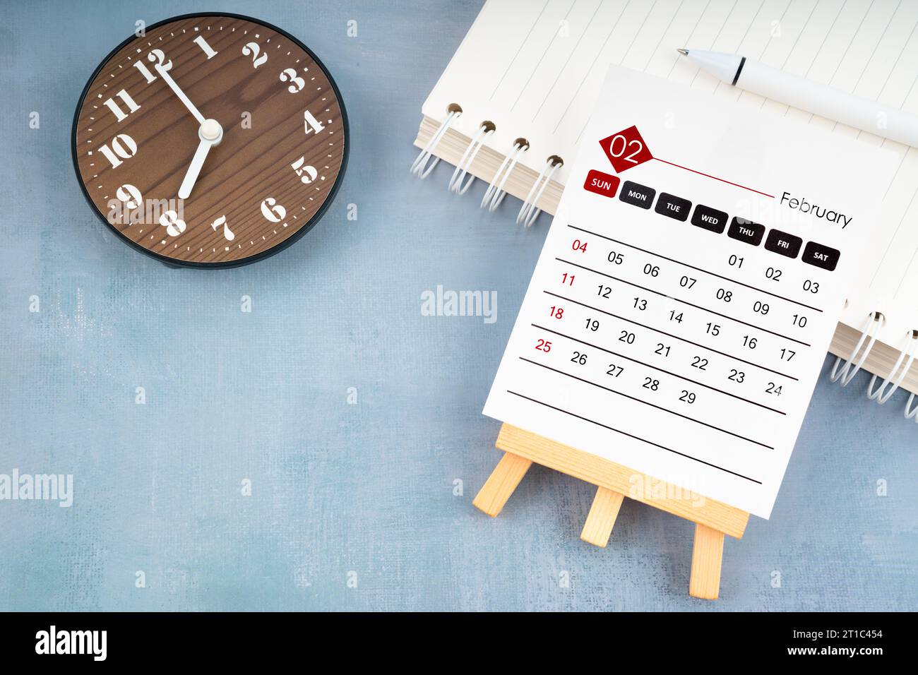 Pagina del calendario del 2024 febbraio e orologio in legno su sfondo di legno blu. Foto Stock