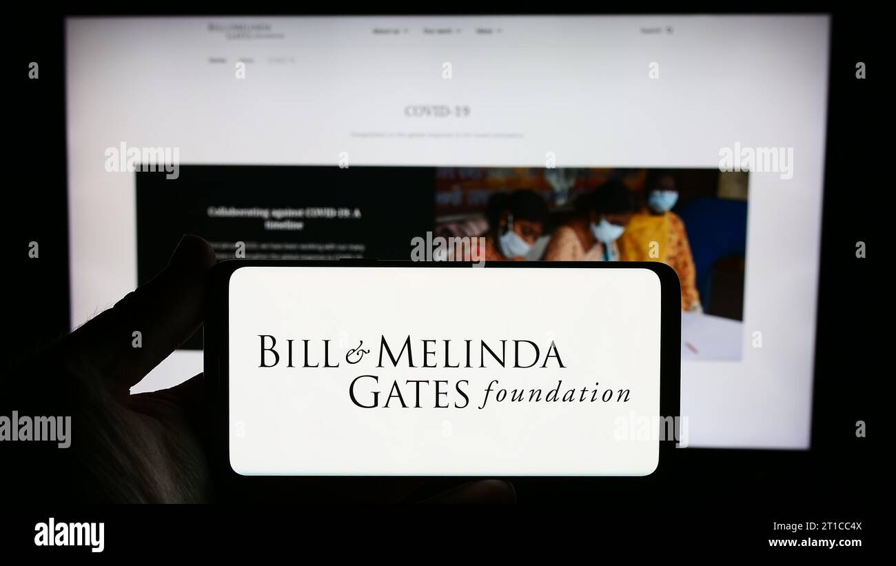 Persona che possiede uno smartphone con il logo dell'American Bill e della Melinda Gates Foundation (BMGF) davanti al sito Web. Concentrarsi sul display del telefono. Foto Stock