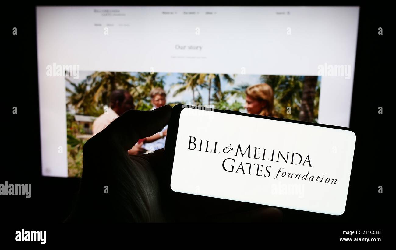 Persona in possesso di un cellulare con il logo dell'American Bill and Melinda Gates Foundation (BMGF) davanti alla pagina web. Concentrarsi sul display del telefono. Foto Stock