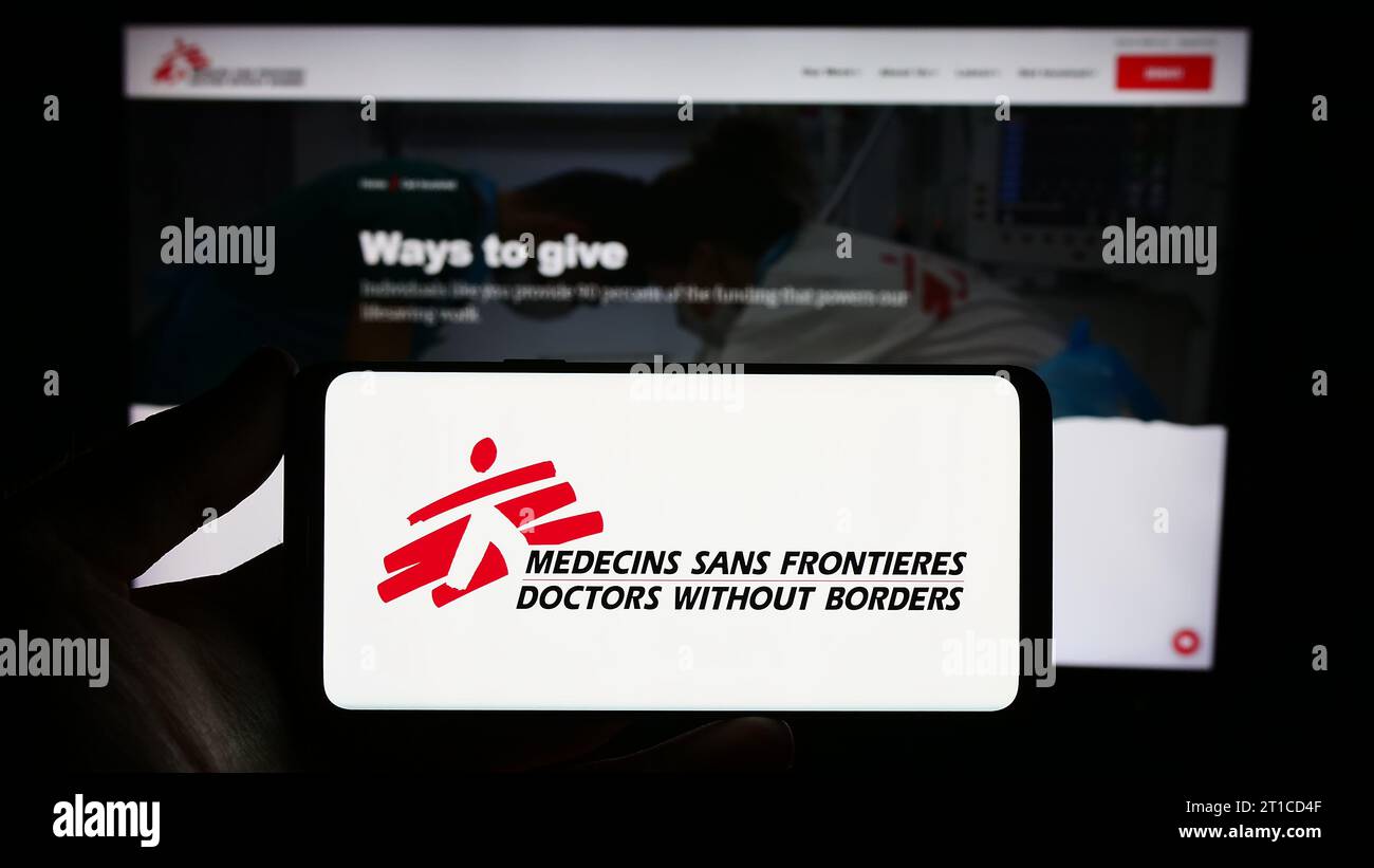 Persona che possiede uno smartphone con il logo dell'organizzazione benefica Doctors Without Borders davanti al sito Web. Concentrarsi sul display del telefono. Foto Stock