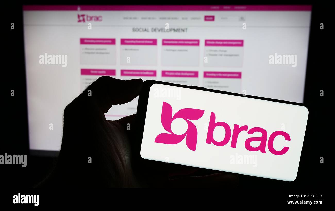 Persona che possiede il cellulare con il logo dell'organizzazione internazionale di sviluppo BRAC davanti alla pagina Web. Concentrarsi sul display del telefono. Foto Stock