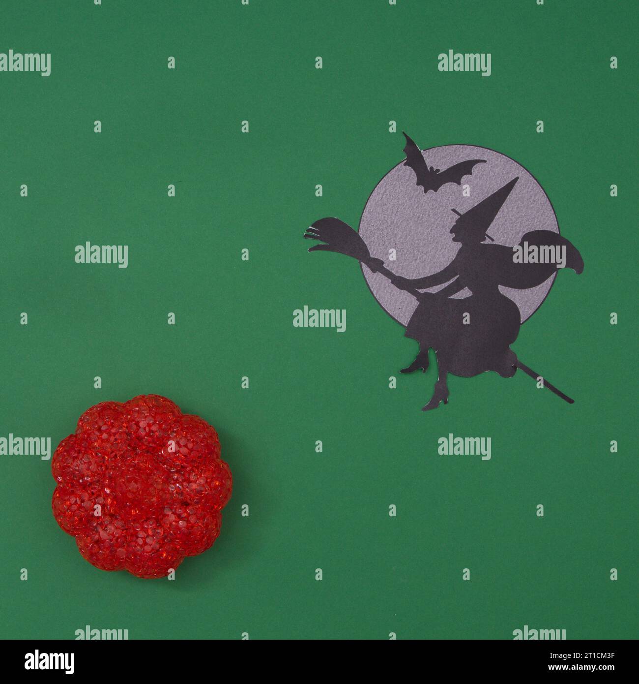 Una strega su una scopa vola accanto alla luna con un pipipistrello sopra la zucca, su uno sfondo verde. Spazio di copia e scenografia piatta minima. Foto Stock