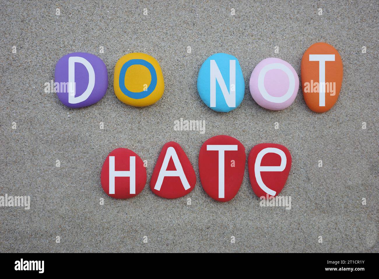 Non odiare, messaggio creativo composto da lettere di pietra multicolore dipinte a mano sulla sabbia della spiaggia Foto Stock