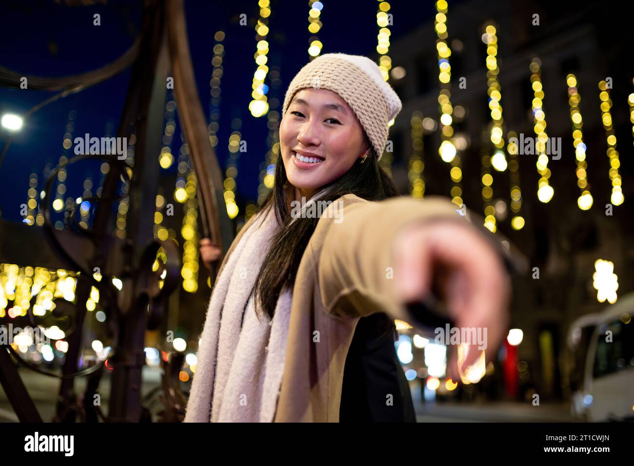 Ragazza sorridente che guarda la fotocamera mentre si gode le luci di natale in strada. Donna spensierata che si diverte di notte in città durante l'inverno. Foto Stock