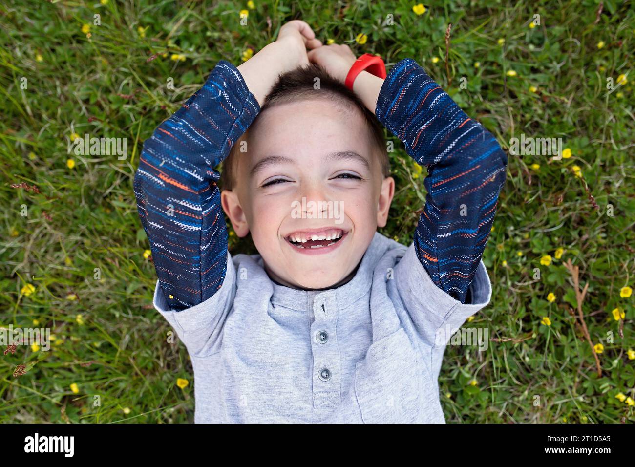 Immagine in alto di un ragazzo che ride nell'erba con i denti mancanti Foto Stock