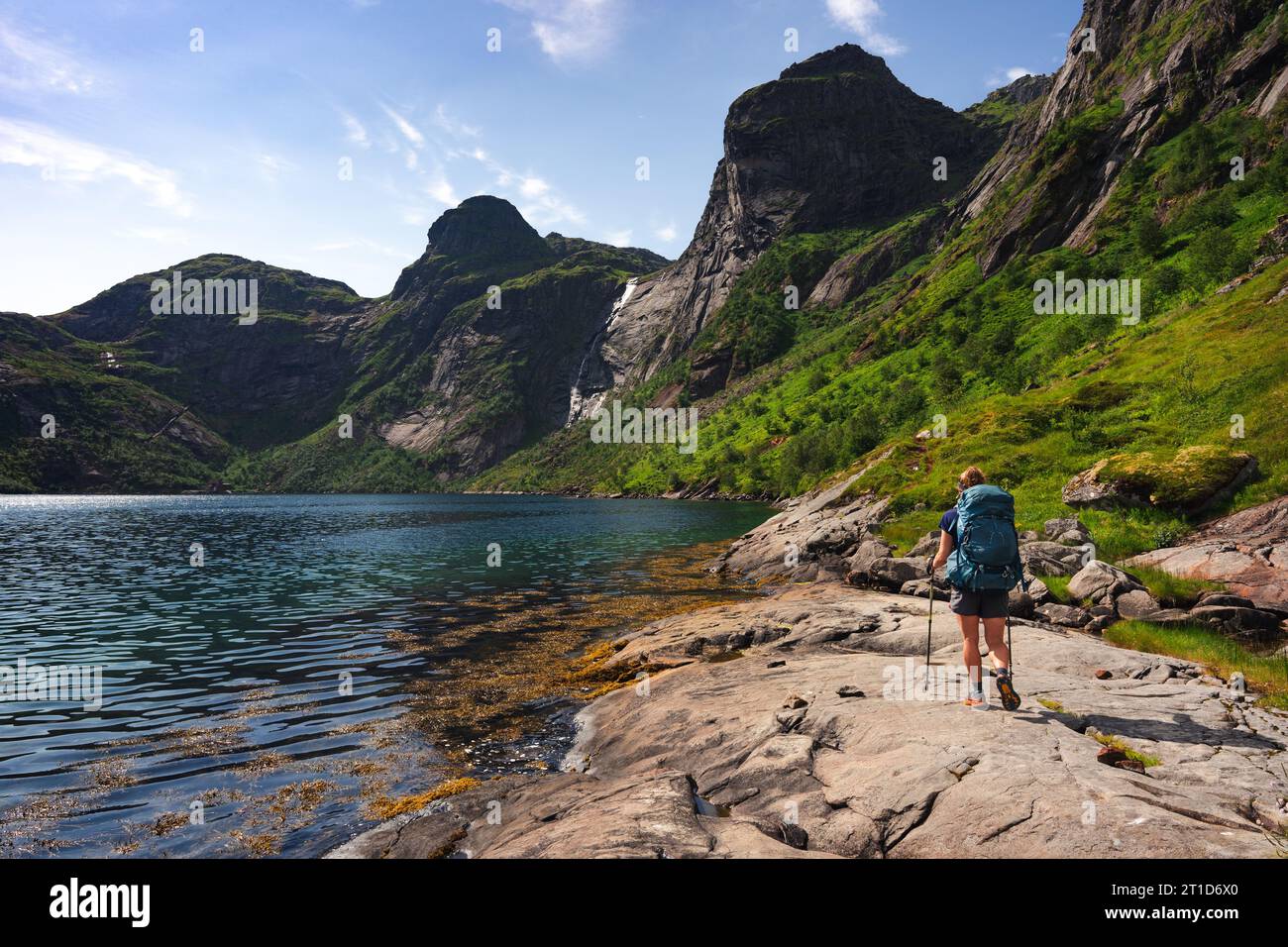 Donna per backpacker lungo il fiordo sotto le montagne Foto Stock