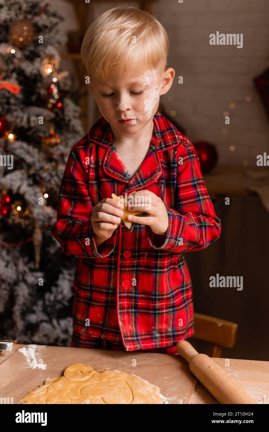 Il ragazzo in pigiama rosso cuoce i biscotti di Natale in cucina. Piccolo chef. Foto di alta qualità Foto Stock