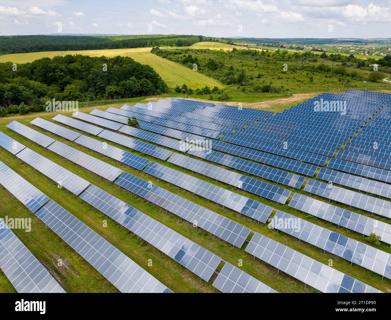 In mezzo a un prato lussureggiante e a una foresta, i pannelli solari sono alti e sfruttano l'energia del sole. Le loro superfici luccicanti riflettono il cielo vibrante, creando un mes Foto Stock