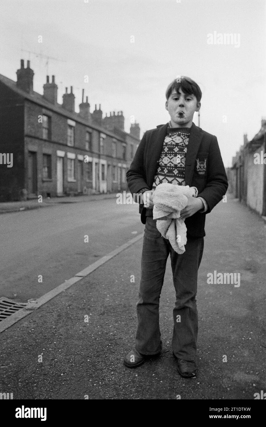 Ragazzo che indossa un blazer scolastico con un distintivo Nottingham Forest e tiene in mano un asciugamano mentre gli tira fuori la lingua, St Ann's, Nottingham. 1969-1972 Foto Stock