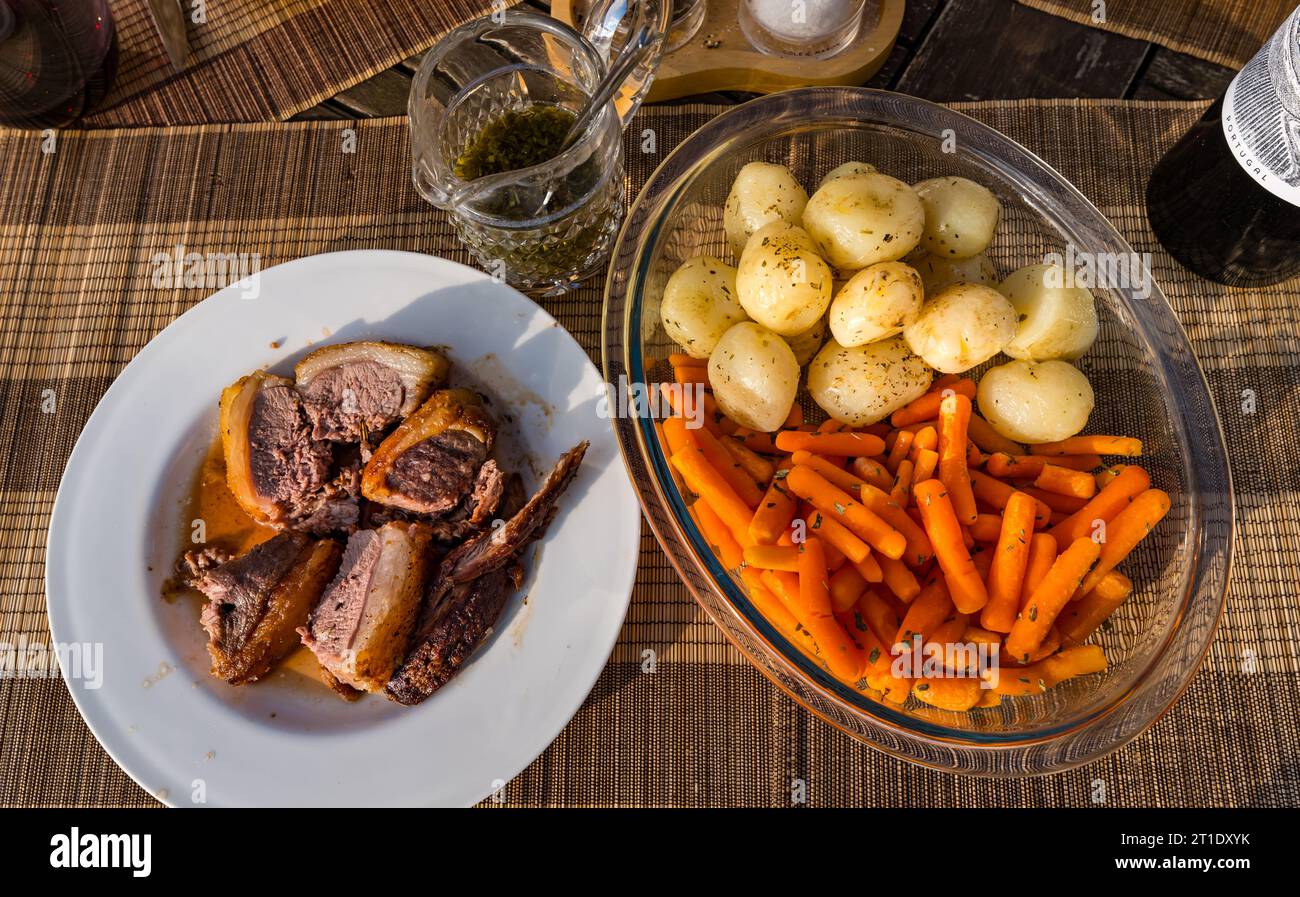Piatto con agnello con salsa alla menta, patate e carote, bottiglia di vino Foto Stock