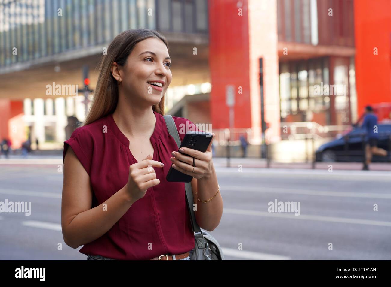 Una donna brasiliana sorridente saluta un veicolo utilizzando un'app mobile in attesa di un taxi o di un uber su Paulista Avenue, San Paolo, Brasile Foto Stock