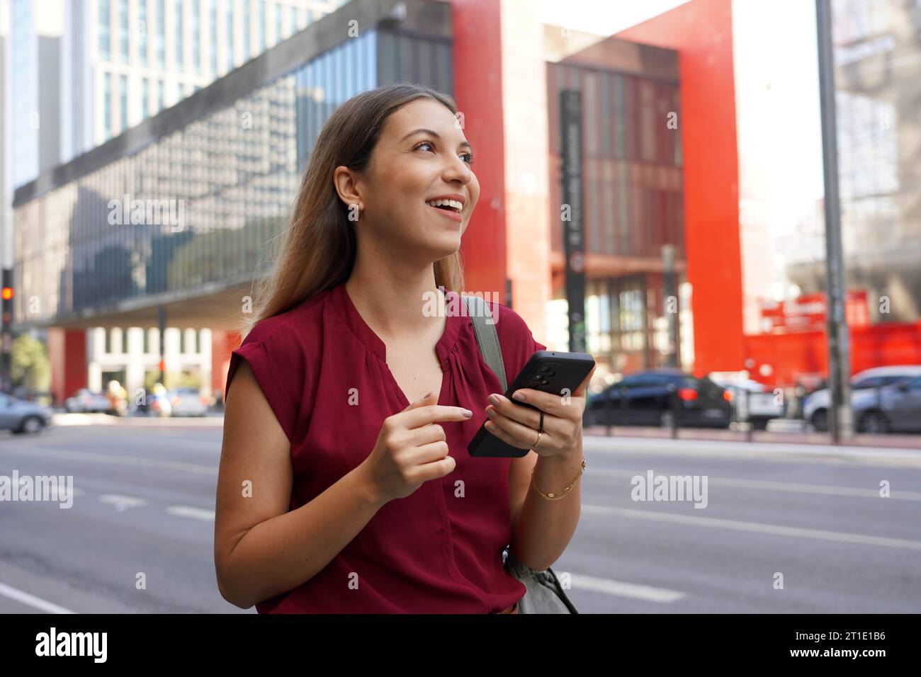 Donna d'affari brasiliana che usa il suo smartphone con il supporto dell'anello che cammina su Paulista Avenue a San Paolo megalopolis, Brasile Foto Stock